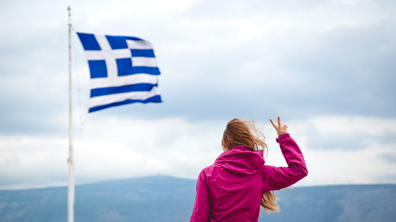 une personne brandissant un geste de paix devant le drapeau grec