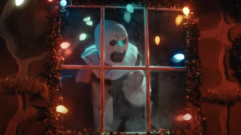 Art Le clown a l'air excité alors qu'il regarde à travers une fenêtre ornée de lumières de Noël dans Terrifiant 3