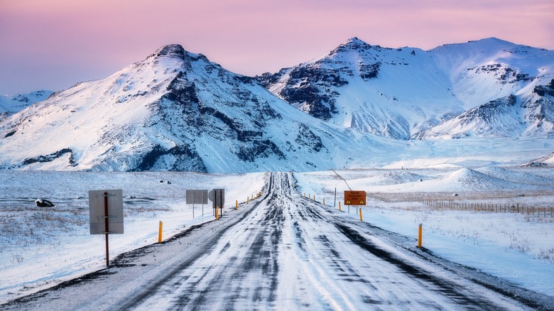 Tracks de véhicules sur Winter Road avec des montagnes enneigées et le coucher du soleil en arrière-plan