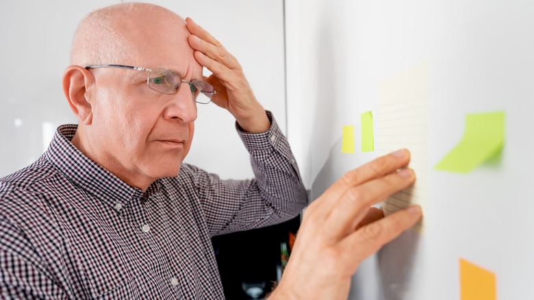 Un homme âgé est montré en tenant la tête et en regardant des notes post-it sur le mur