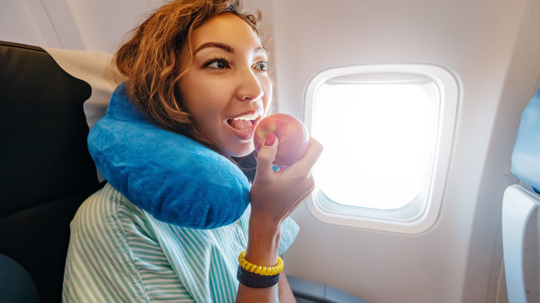 Un voyageur d'avion mord une pomme.