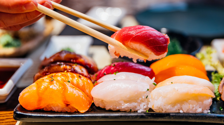 Une personne saisit un gros morceau de sushis avec une paire de baguettes en bois