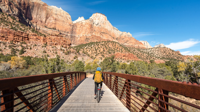 Femme à vélo sur un pont devant les falaises au parc national de Zion