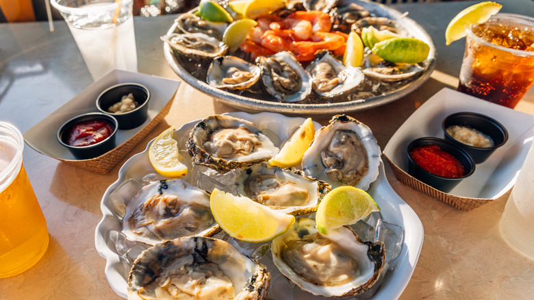 Assiettes d'huîtres fraîches et de crevettes avec sauce et boissons.