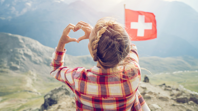 Femme suisse faisant un geste de cœur avec le drapeau suisse en arrière-plan