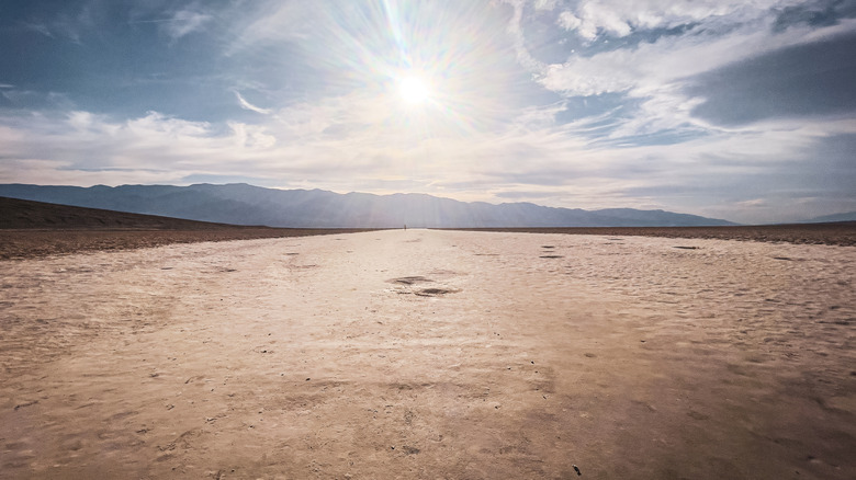 Le paysage du désert stérile de Death Valley est vu sous un ciel nuageux avec un soleil brillant qui brille à travers