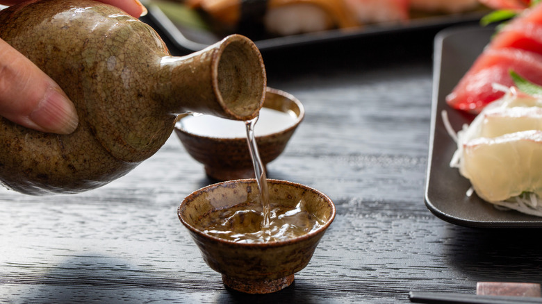 Quelqu'un verse au saké dans une petite tasse à côté de la plaque de sushis