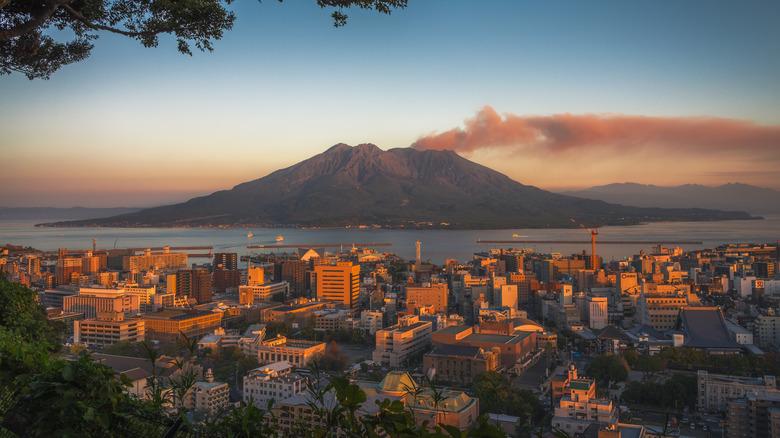 Un volcan à travers un lac avec des bâtiments à la lumière du coucher du soleil au premier plan