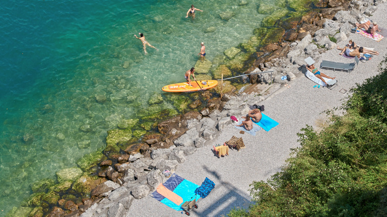 Paddleboarders et chaises longues sur une plage de galets sur le lac Garda