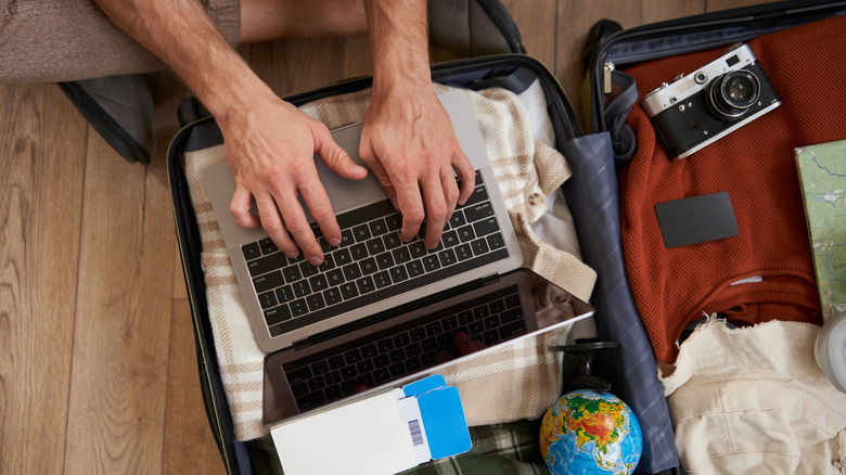 Mains tapant sur un ordinateur portable sur une valise emballée.