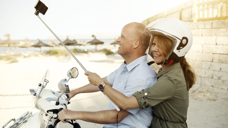 Un homme et une femme montent un scooter avec un bâton de selfie