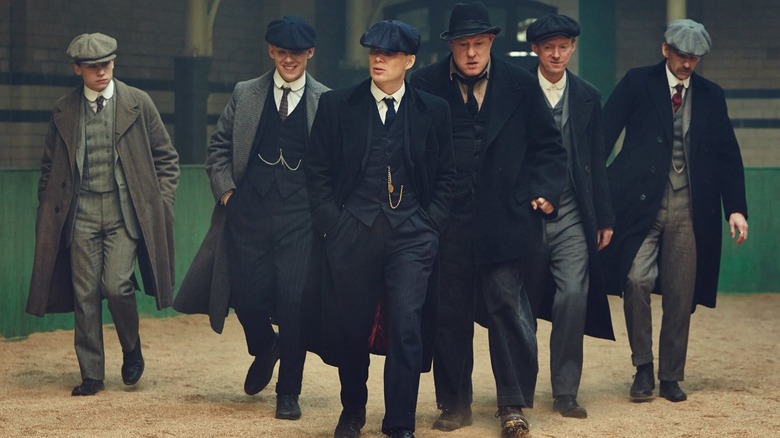 Cillian Murphy comme Tommy Shelby, Paul Anderson comme Arthur Shelby, Finn Cole comme Michael Gray, et d'autres membres du gang Shelby marchant de manière affrontement à Peaky Blinders