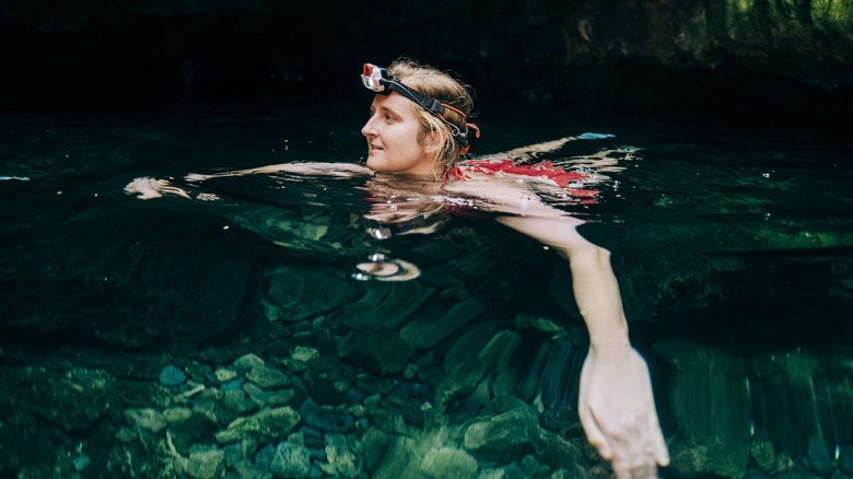 Femme nageant dans la grotte avec la lampe frontale