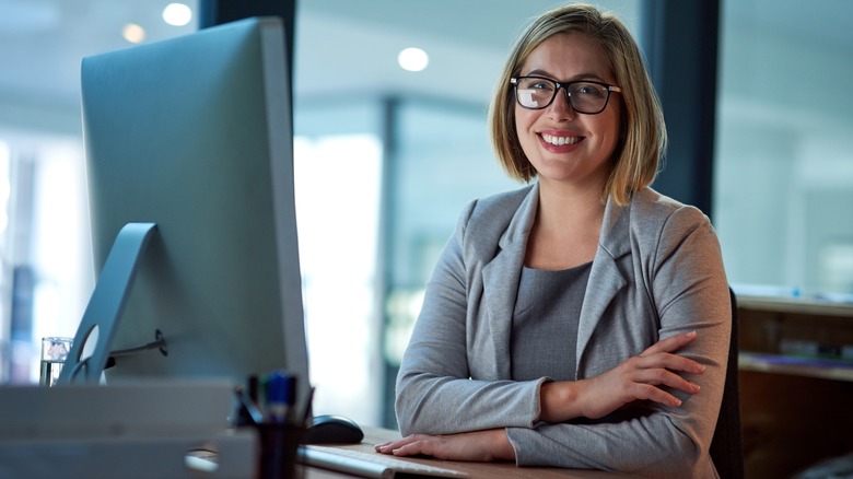 Une femme à lunettes sourit près de son ordinateur