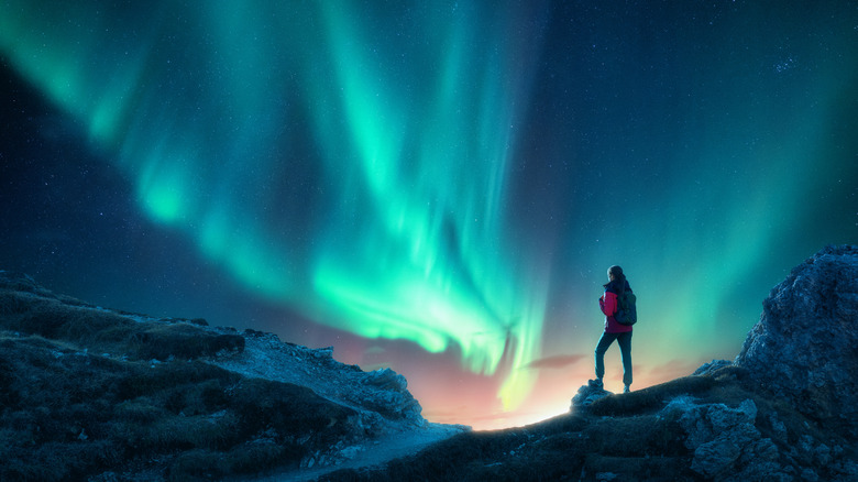 Silhouette d'un routard debout sur une colline ou un sommet de montagne sous l'Aurora Borealis