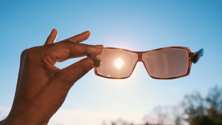 La main d'une femme tient des lunettes de soleil contre le ciel avec le soleil visible à travers l'objectif