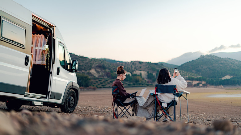 couple assis dans des chaises à côté de camping-car avec fond de montagne