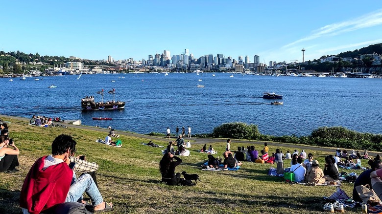 Pelouse en pente avec des gens, la baie de l'eau avec des bateaux et des toits