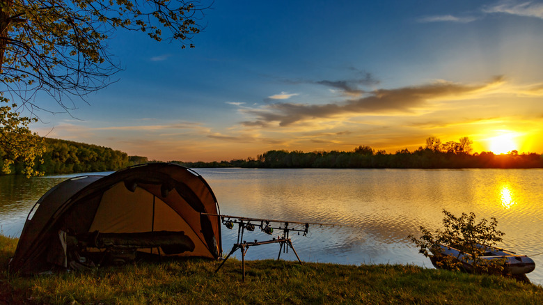 Pôles de tente et de pêche au bord du lac avec bateau au coucher du soleil