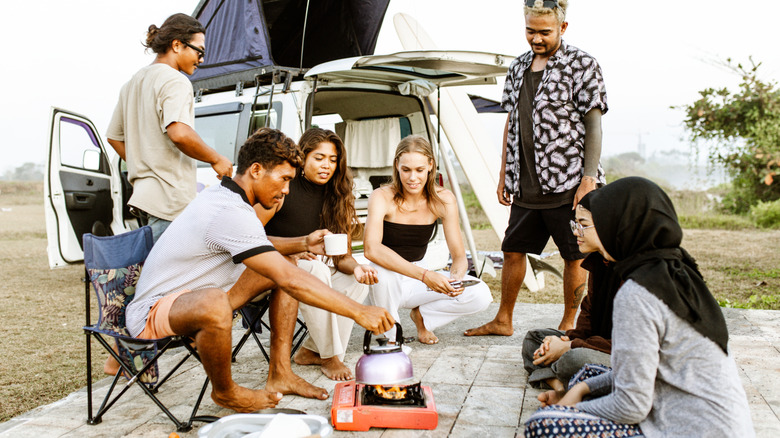 Un groupe diversifié de jeunes voyageurs cuisine devant un camping-car