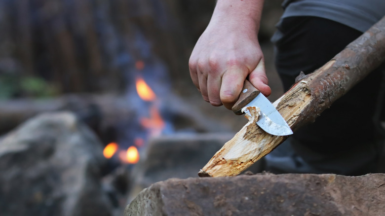 Un homme sculpte un morceau de bois avec un couteau de camping