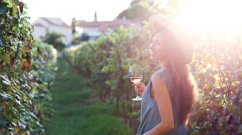 Une femme marche dans un vignoble avec un verre de vin