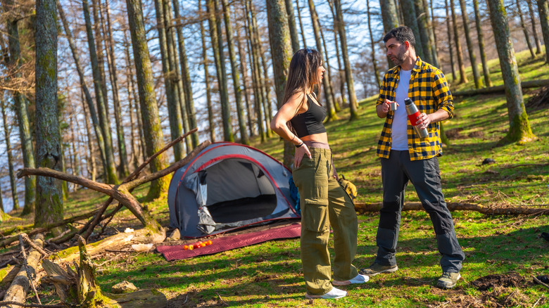 Un homme et une femme conversent près d'une tente dans les bois
