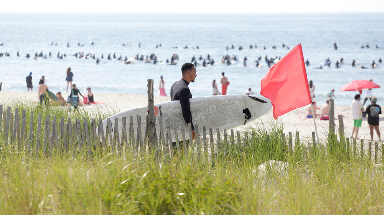 Un surfeur se dirigeant vers le rivage à Rockaway Beach près d'un drapeau rouge