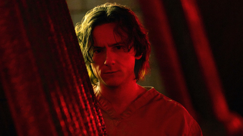 Bob Reynolds debout partiellement dissimulé en éclairage rouge dans les coups de foudre