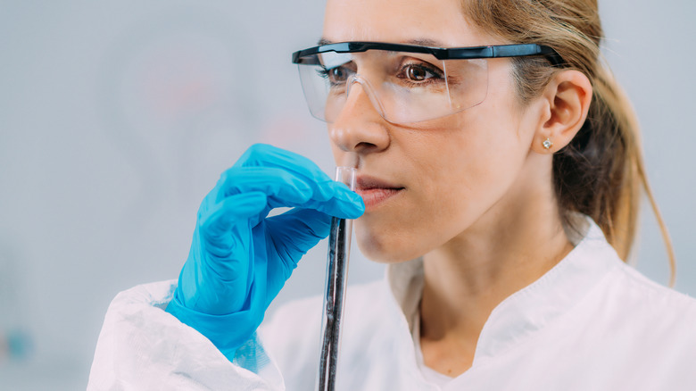 Femme en laboratoire avec des gants et des verres de sécurité sentant un flacon