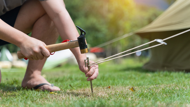 Quelqu'un martèle une cheville de tente dans un sol herbeux