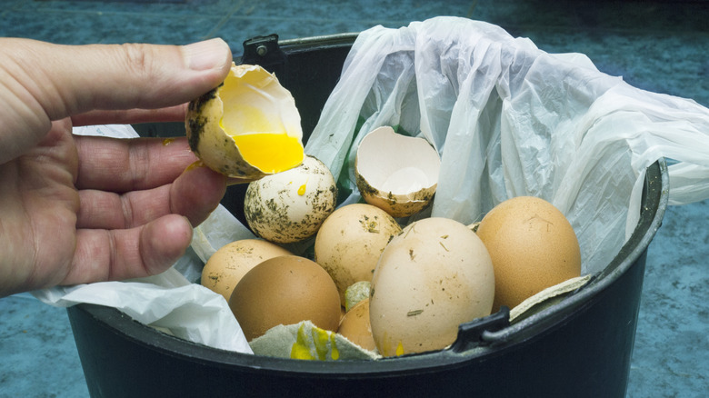 Main tenant un œuf cassé sur une poubelle pleine d'œufs