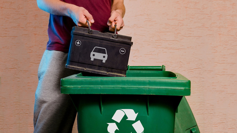 Homme plaçant une batterie de voiture traditionnelle dans une poubelle verte