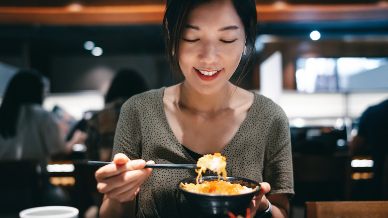 Une femme japonaise soulève son bol de la table dans un restaurant