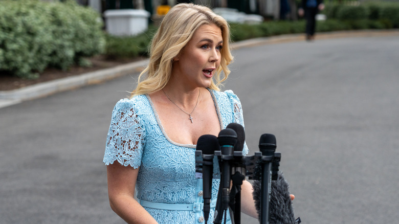 Karoline Leavitt dans une robe en dentelle bleue derrière un podium en avril 2025