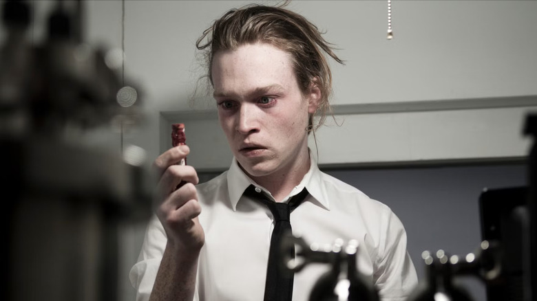 Un Syd March à l'air érectueux regarde un petit objet rouge qu'il tient dans sa main en antiviral