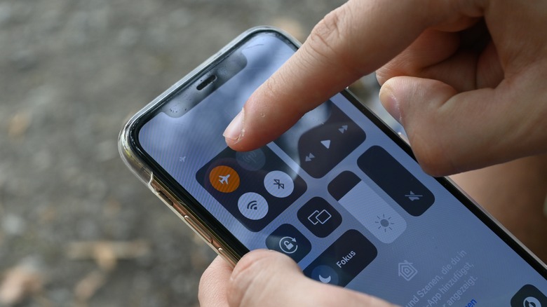 Gros plan d'une personne qui tape l'icône du mode avion sur un iPhone