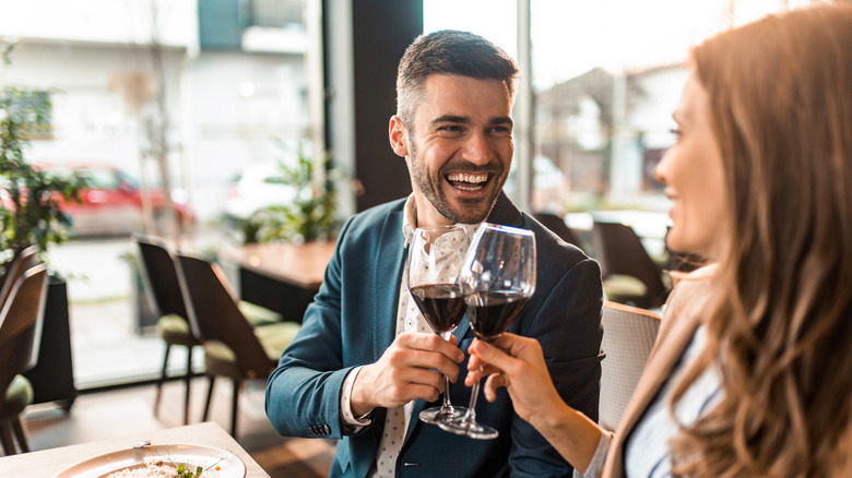 Heureux jeune homme grillant de vin tout en déjeunant avec sa petite amie dans un restaurant