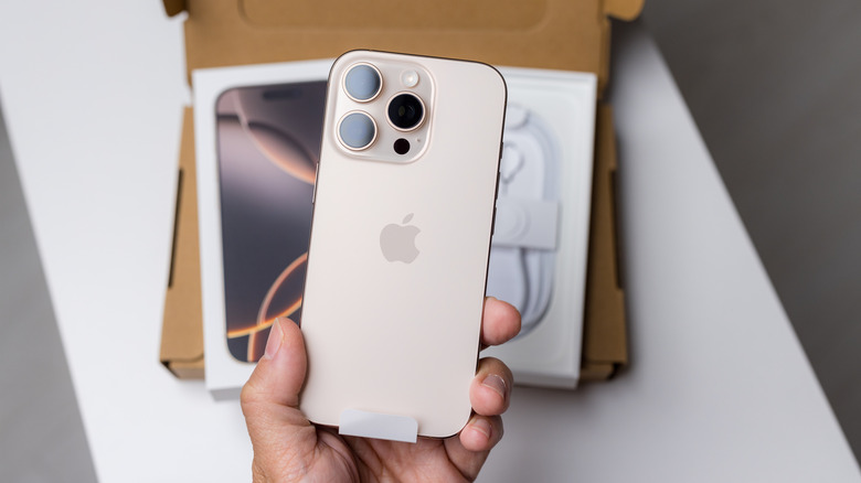 Une main tenant un iPhone Pro Max avec une boîte en arrière-plan