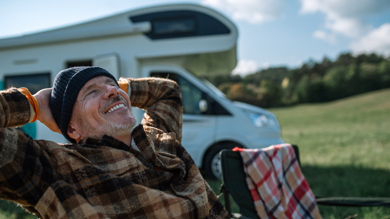 Un homme se détend et sourit devant son camping-car.