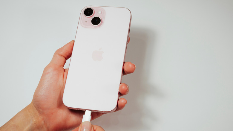 Personne tenant un iPhone blanc et branchant le chargeur