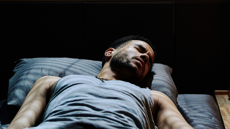 Un homme est dans son lit illuminé par la lumière à travers des stores