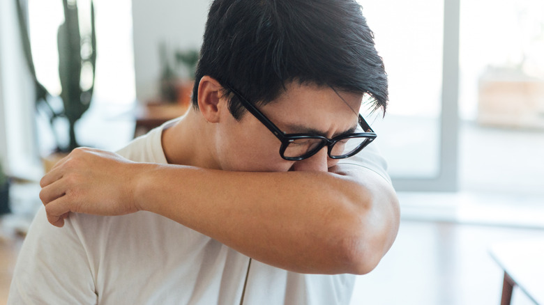Un homme tient son bras sur son visage pendant qu'il éternue