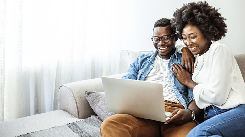Un couple regarde affectueusement un ordinateur tandis que vous assis sur un canapé
