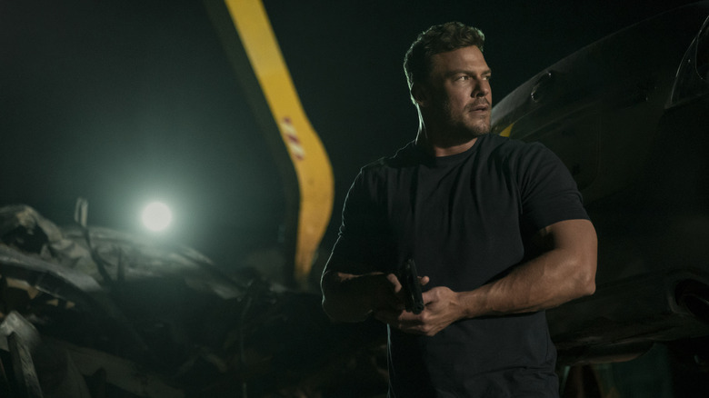 Alan Ritchson en tant que Jack Reacher tenant un pistolet au milieu d'une fusillade dans la saison 3 de Reachor