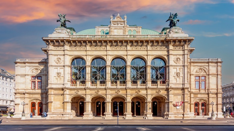 Grand bâtiment avec des statues sur le toit au coucher du soleil