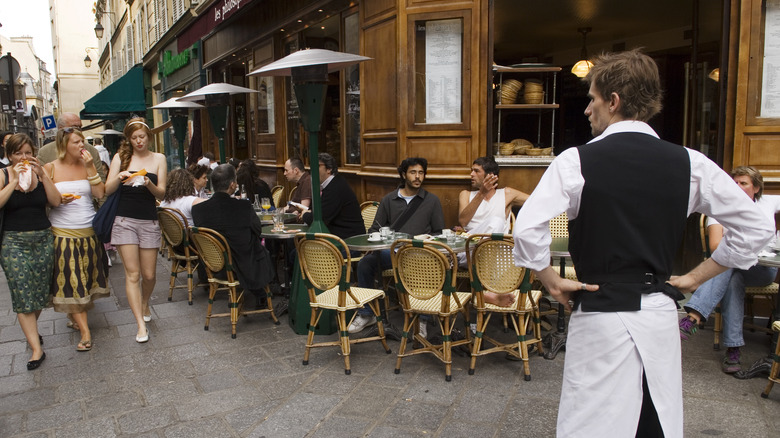 un serveur avec des bras akimbo devant un café