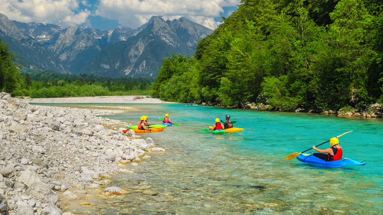 Un groupe de kayakers sur une rivière turquoise avec des montagnes et des forêts vertes