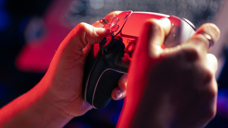 Une personne tenant un contrôleur PS5 sous la lumière rouge.