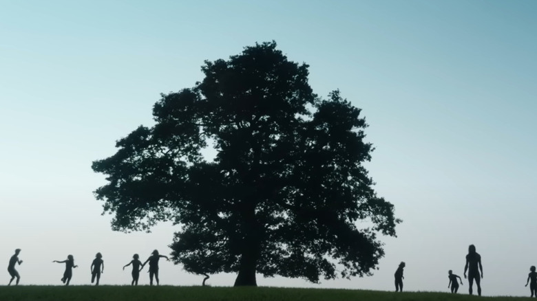 Un coup de silhouette de plusieurs personnes infectées par un arbre sur une colline dans 28 ans plus tard